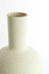 Nahaufnahme einer cremefarbenen Vase mit geriffelter Oberfläche und schmalem Hals, seitliche Perspektive.
