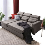 Graue Rundecke mit verstellbaren Kopfstützen, dekoriert mit Kissen und Decke, aus der Perspektive von vorne links.