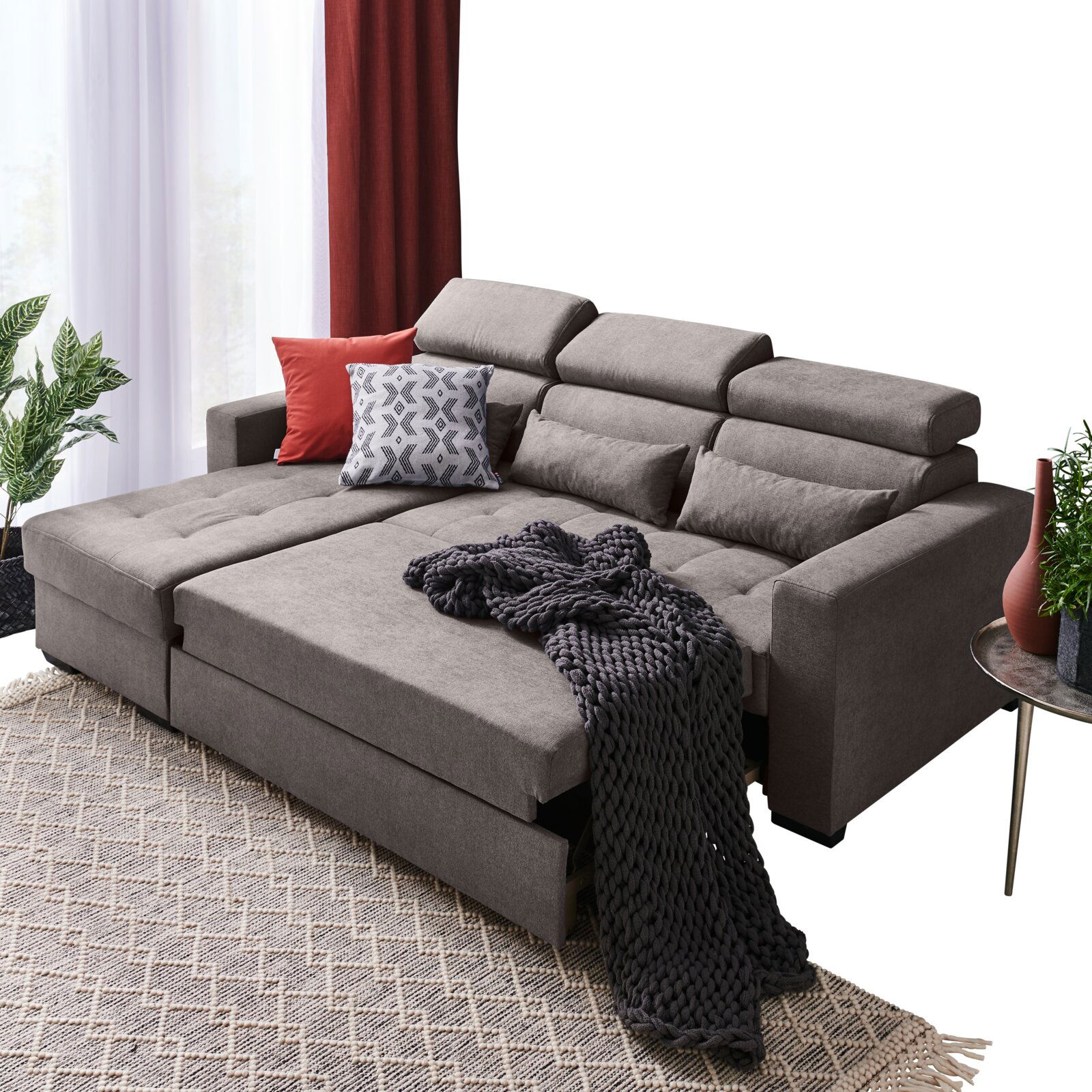 Graue Rundecke mit verstellbaren Kopfstützen, dekoriert mit Kissen und Decke, aus der Perspektive von vorne links.