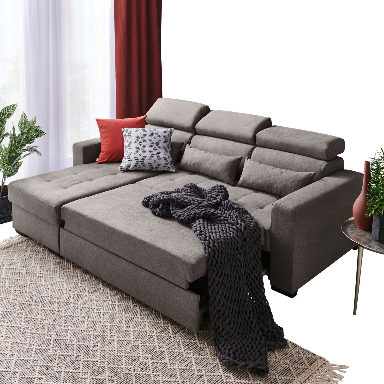 Graue Rundecke mit verstellbaren Kopfstützen, dekoriert mit Kissen und Decke, aus der Perspektive von vorne links.