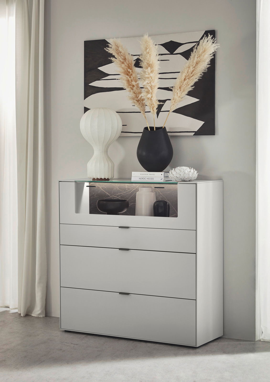Dieter Knoll Hoogkast MONTESA Modernes Highboard in Weiß mit drei Schubladen, dekoriert mit einer schwarzen Vase und Pampasgras, aus seitlicher Perspektive fotografiert.