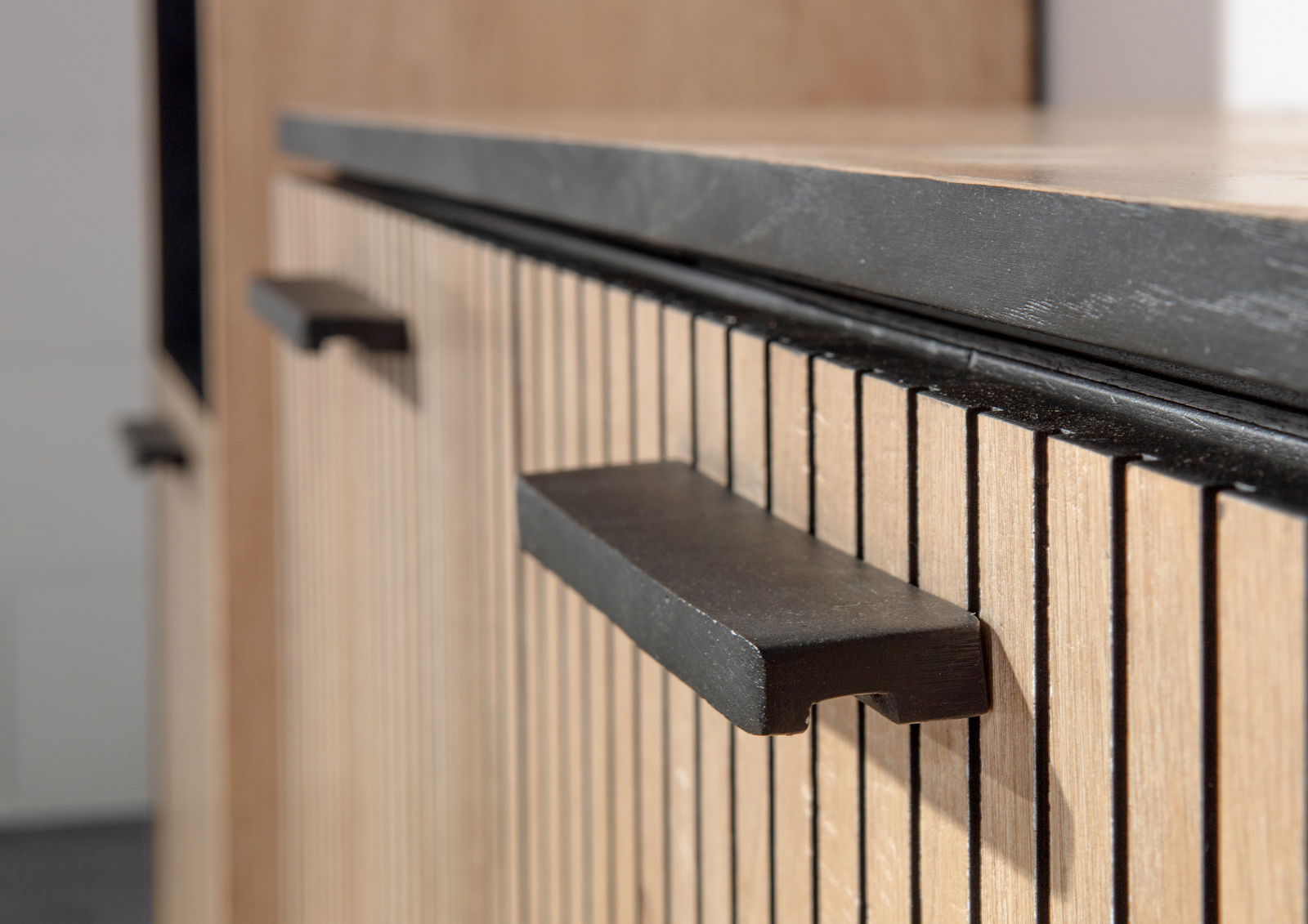 Nahaufnahme eines Möbelstücks mit vertikalen Holzlamellen und schwarzen Griffen, seitliche Perspektive