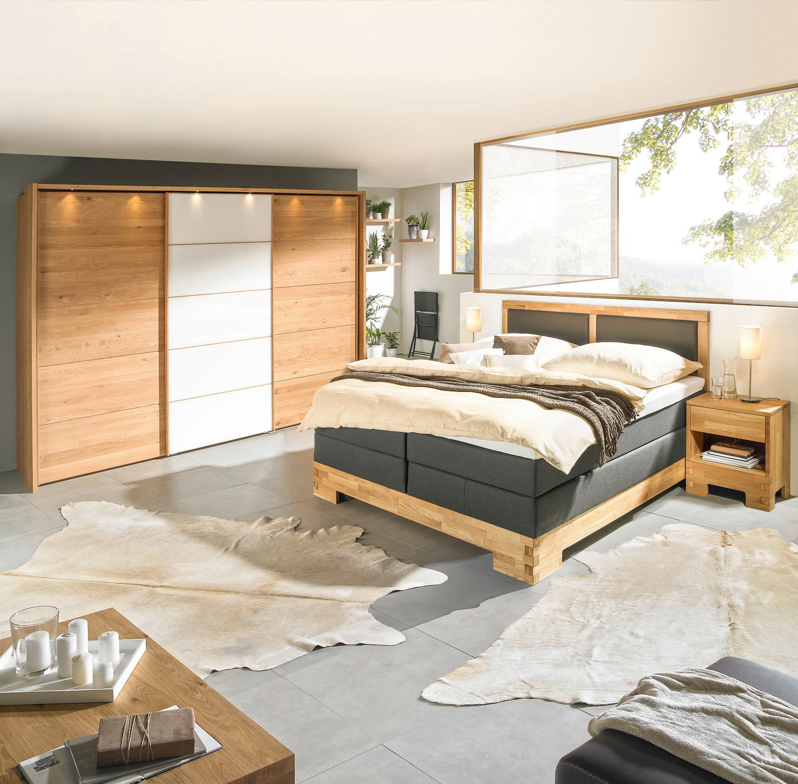Modernes Schlafzimmer mit Boxspringbett, Nachtkommode und großem Kleiderschrank aus Holz, seitliche Perspektive.