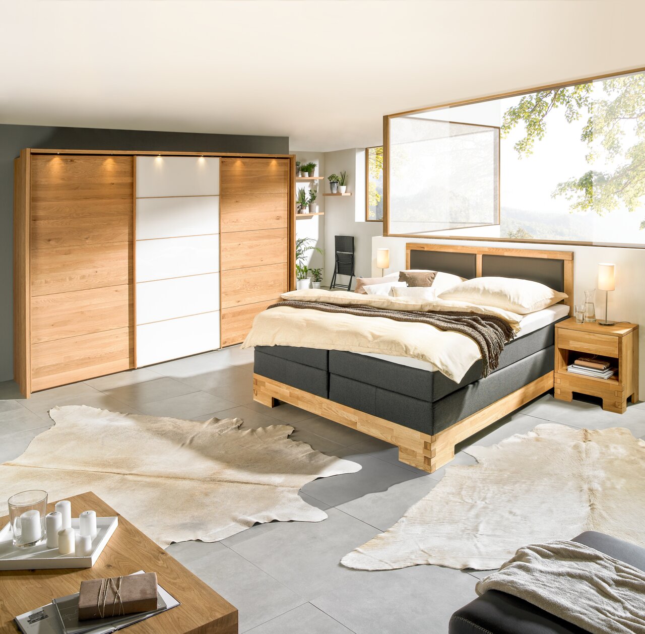 Modernes Schlafzimmer mit Boxspringbett, Nachtkommode und großem Kleiderschrank aus Holz, seitliche Perspektive.