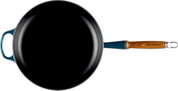 Bovenaanzicht van een zwarte gietijzeren koekenpan met blauwgroene buitenkant, houten steel met Le Creuset-logo en een extra handgreep aan de overzijde