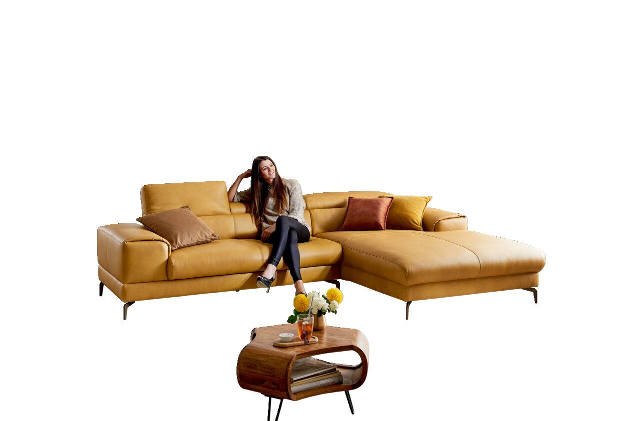 Gelbes Longchair-Sofa mit Kissen, auf dem eine Frau sitzt, aus frontaler Perspektive. Im Vordergrund ein kleiner Holztisch mit Blumen.