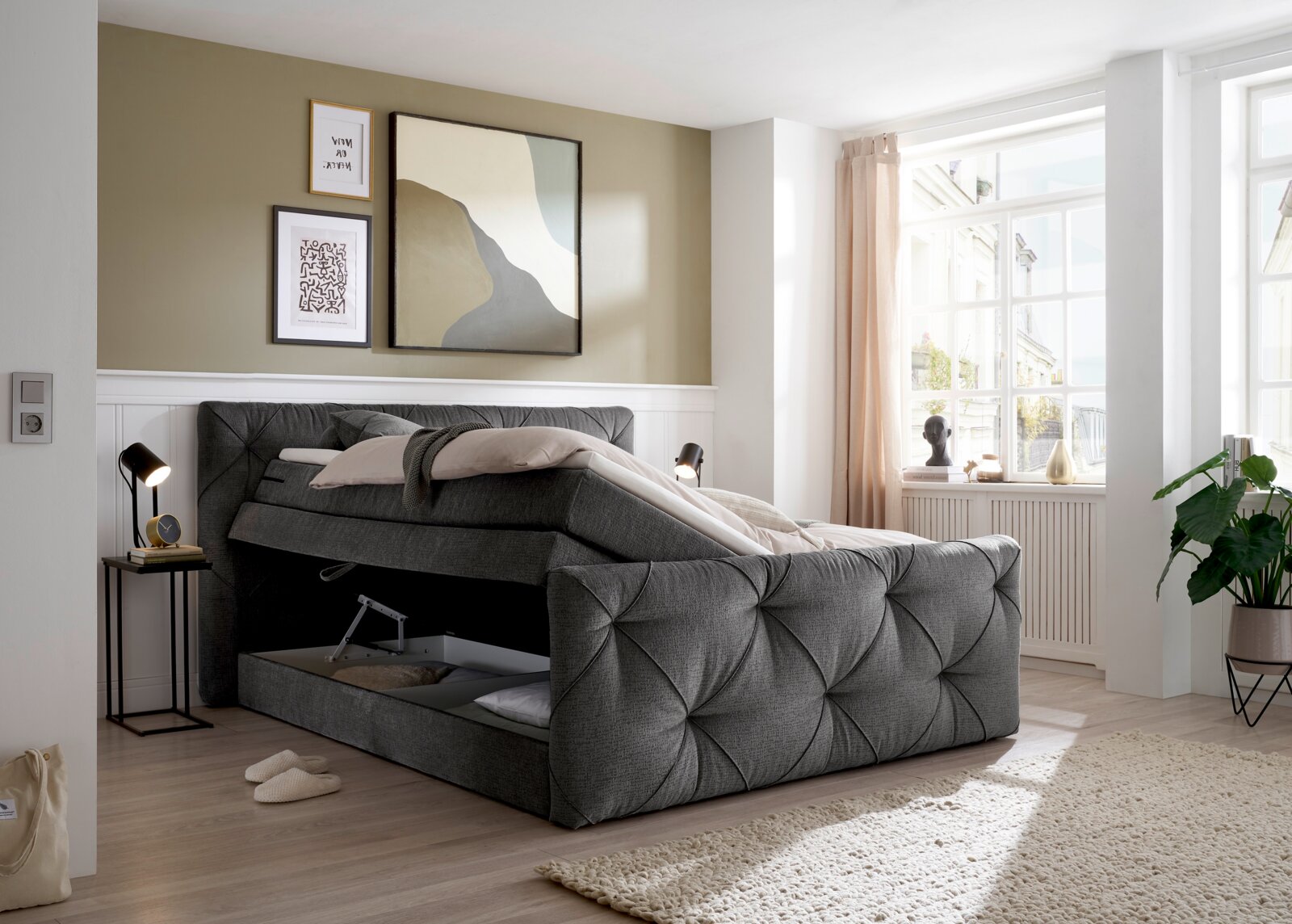 Grijs boxspringbed met opbergruimte, gezien vanaf de zijkant, in een moderne slaapkamer met grote ramen en een stijlvolle inrichting.