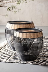 Zwei runde Beistelltische aus schwarzem Metall und hellem Rattan, auf einem gemusterten Teppich stehend, seitliche Perspektive.