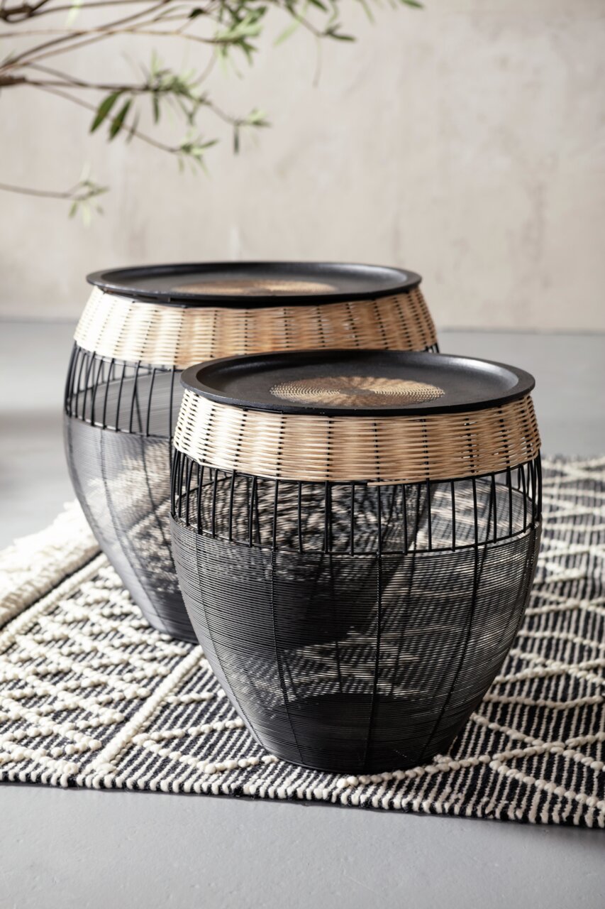 Zwei runde Beistelltische aus schwarzem Metall und hellem Rattan, auf einem gemusterten Teppich stehend, seitliche Perspektive.