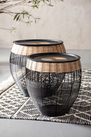Zwei runde Beistelltische aus schwarzem Metall und hellem Rattan, auf einem gemusterten Teppich stehend, seitliche Perspektive.