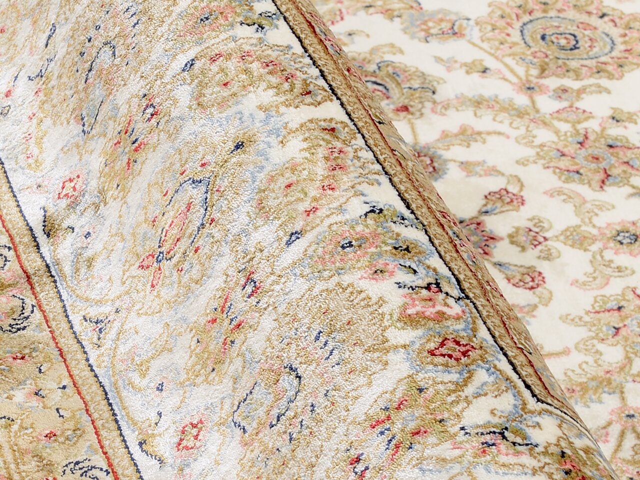 Nahaufnahme eines Orientteppichs mit floralen Mustern in Beige, Rot und Blau. Der Teppich ist teilweise aufgerollt, was die Textur und das detaillierte Design hervorhebt.