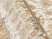 Nahaufnahme eines Orientteppichs mit floralen Mustern in Beige, Rot und Blau. Der Teppich ist teilweise aufgerollt, was die Textur und das detaillierte Design hervorhebt.