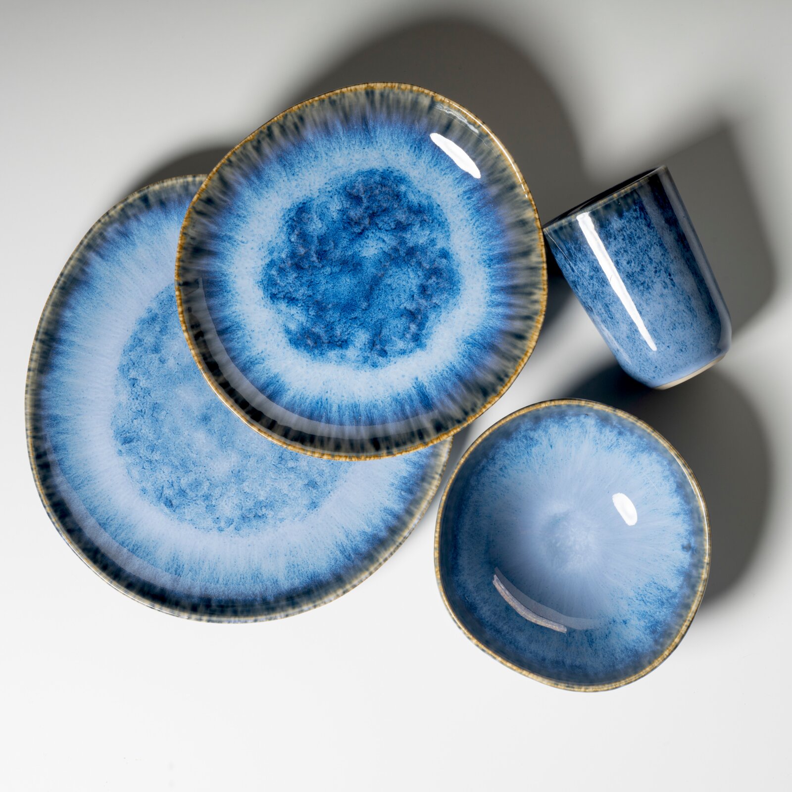 Blau glasiertes Keramik-Geschirrset mit Teller, Schale und Becher, Draufsicht von oben auf hellem Hintergrund