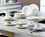 Ein 30-teiliges weißes Geschirrset, bestehend aus Tellern, Tassen und Schalen, auf einer Küchenarbeitsplatte präsentiert. Perspektive von oben.