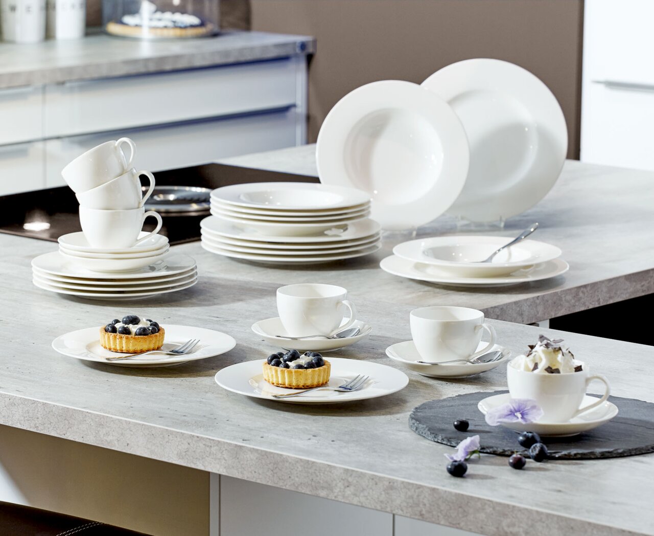 Villeroy & Boch Kombiservice Basic White 30-tlg. Ein 30-teiliges weißes Geschirrset, bestehend aus Tellern, Tassen und Schalen, auf einer Küchenarbeitsplatte präsentiert. Perspektive von oben.