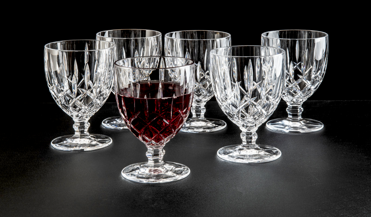 Sechs elegante Weinkelche aus Kristallglas, einer davon mit Rotwein gefüllt, auf schwarzem Hintergrund. Frontale Perspektive.