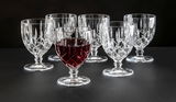 Sechs elegante Weinkelche aus Kristallglas, einer davon mit Rotwein gefüllt, auf schwarzem Hintergrund. Frontale Perspektive.