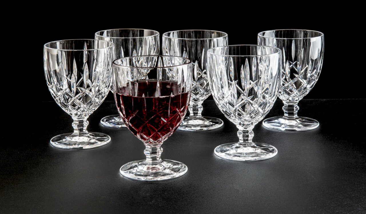 Zes elegante wijnglazen van kristal, waarvan één gevuld met rode wijn, tegen een zwarte achtergrond. Vooraanzicht.
