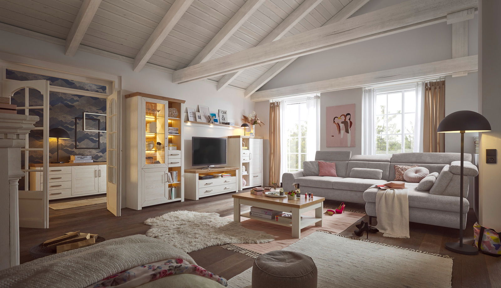 Wohnzimmer mit gemütlicher Einrichtung, bestehend aus einem großen Ecksofa, einem Couchtisch und einer Wohnwand mit Vitrine und TV-Element. Die Perspektive zeigt den Raum von vorne mit Blick auf die gesamte Einrichtung.