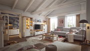 Wohnzimmer mit gemütlicher Einrichtung, bestehend aus einem großen Ecksofa, einem Couchtisch und einer Wohnwand mit Vitrine und TV-Element. Die Perspektive zeigt den Raum von vorne mit Blick auf die gesamte Einrichtung.