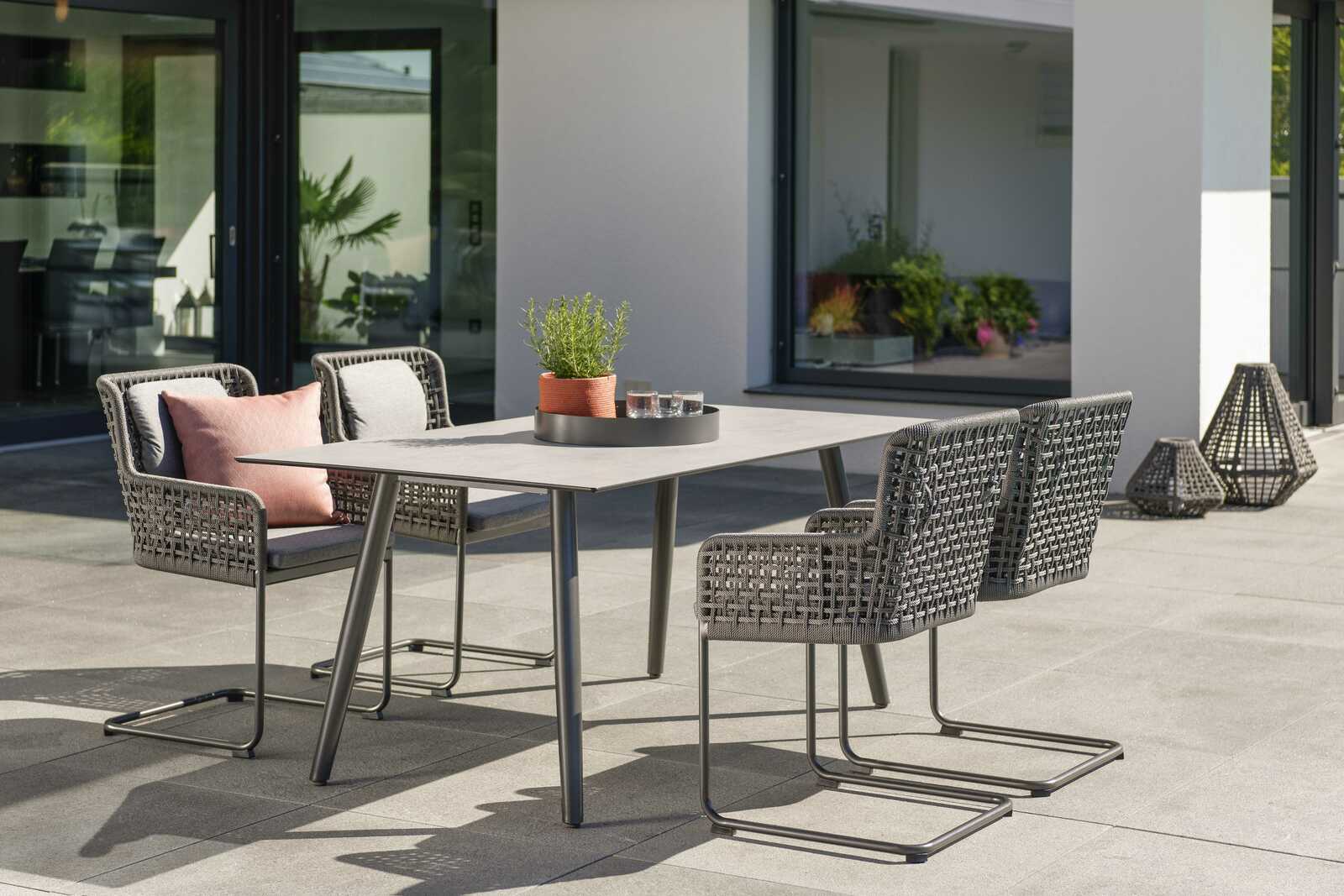 Moderner Freischwinger-Stuhl aus geflochtenem Material auf einer Terrasse, seitliche Perspektive.