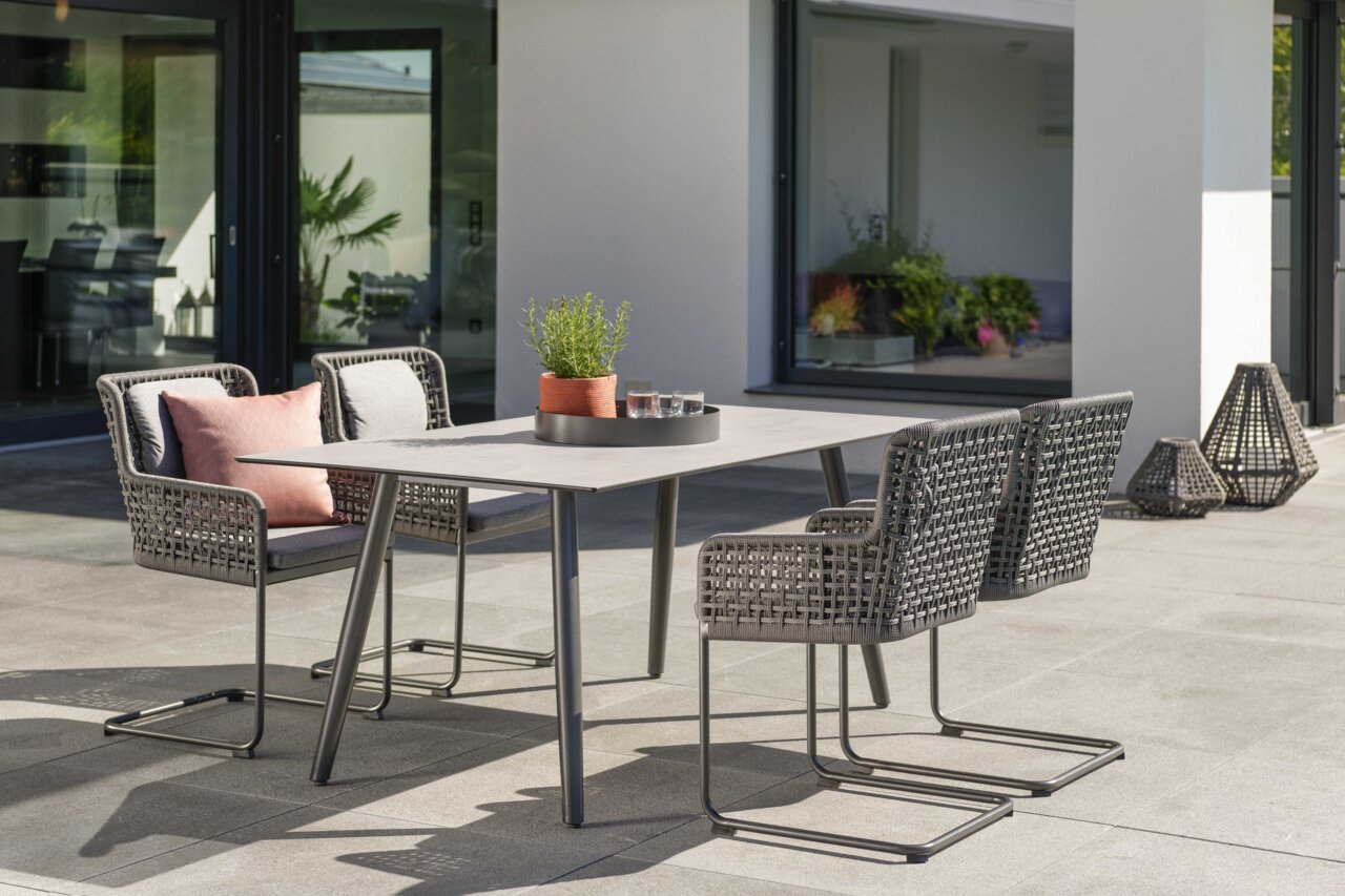 Moderner Freischwinger-Stuhl aus geflochtenem Material auf einer Terrasse, seitliche Perspektive.