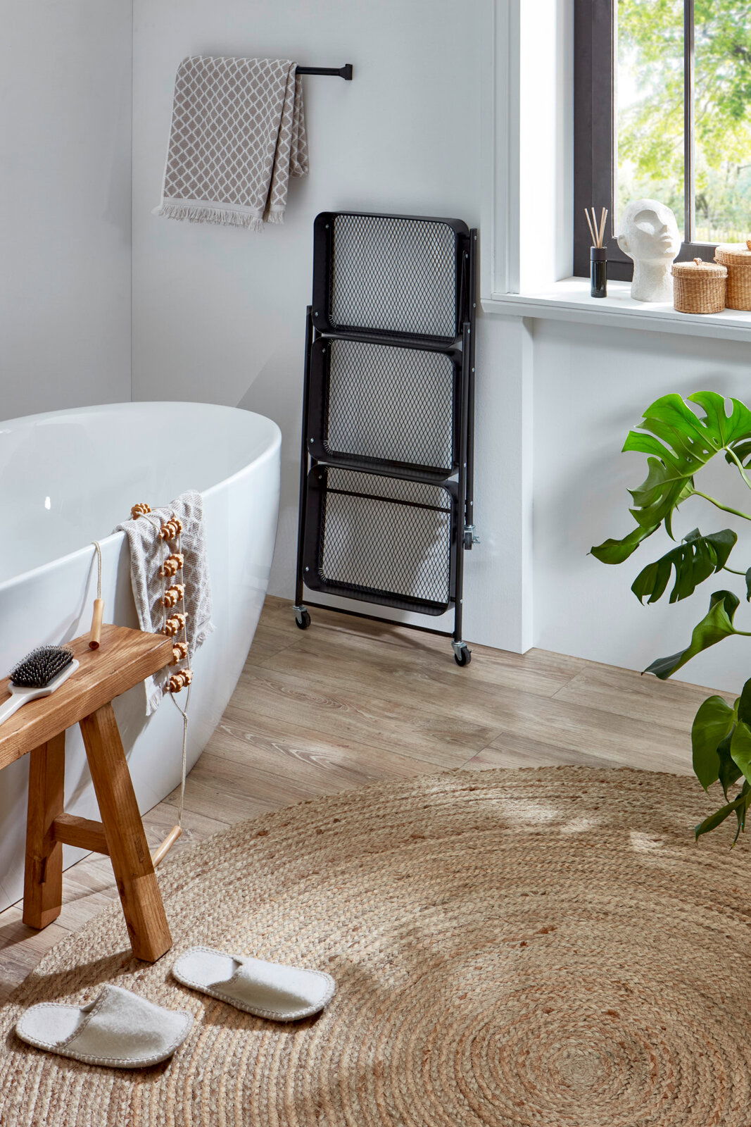 Schwarzer, klappbarer Metall-Wäschekorb mit drei Mesh-Fächern auf Rollen im Badezimmer neben freistehender Badewanne, Frontansicht in leichter Schrägperspektive.