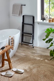 Schwarzer, klappbarer Metall-Wäschekorb mit drei Mesh-Fächern auf Rollen im Badezimmer neben freistehender Badewanne, Frontansicht in leichter Schrägperspektive.