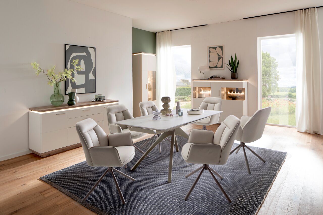 Zurbrüggen Dressoir Palermo Eetkamer met een moderne eettafel en zes gestoffeerde stoelen, omringd door dressoirs en hoge kasten met ledverlichting, gezien vanuit een open, lichte ruimte met uitzicht naar buiten.