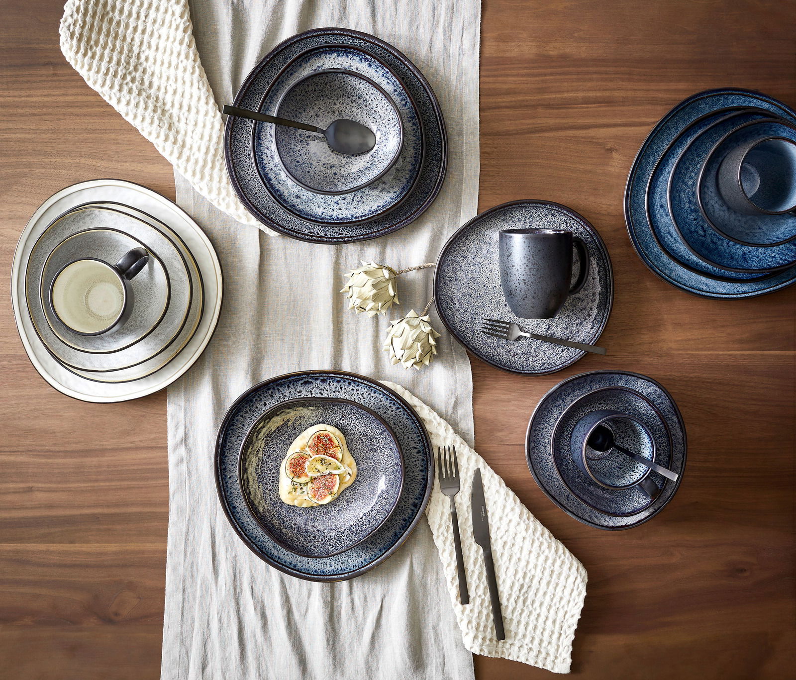 Vogelperspektive auf ein stilvolles, graues Kombiset Sören mit 10 Teilen, bestehend aus Tellern, Tassen und Schalen, auf einem Holztisch mit Tischläufer arrangiert.