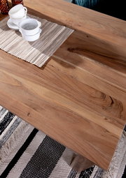 Nahaufnahme eines Esstisches aus Holz mit natürlicher Maserung, darauf stehen weiße Tassen und Schalen auf einem gestreiften Tischläufer, Perspektive von oben.