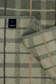 Detailaufnahme von oben auf ein JOOP! Frottier-Handtuch mit kariertem Muster und Blättermotiv in Grün- und Beigetönen, mit eingefasster Kante und Markenlabel