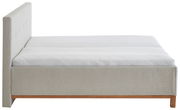 Seitliche Ansicht eines modernen Polsterbetts mit hellem Stoffbezug und Holzfuß.