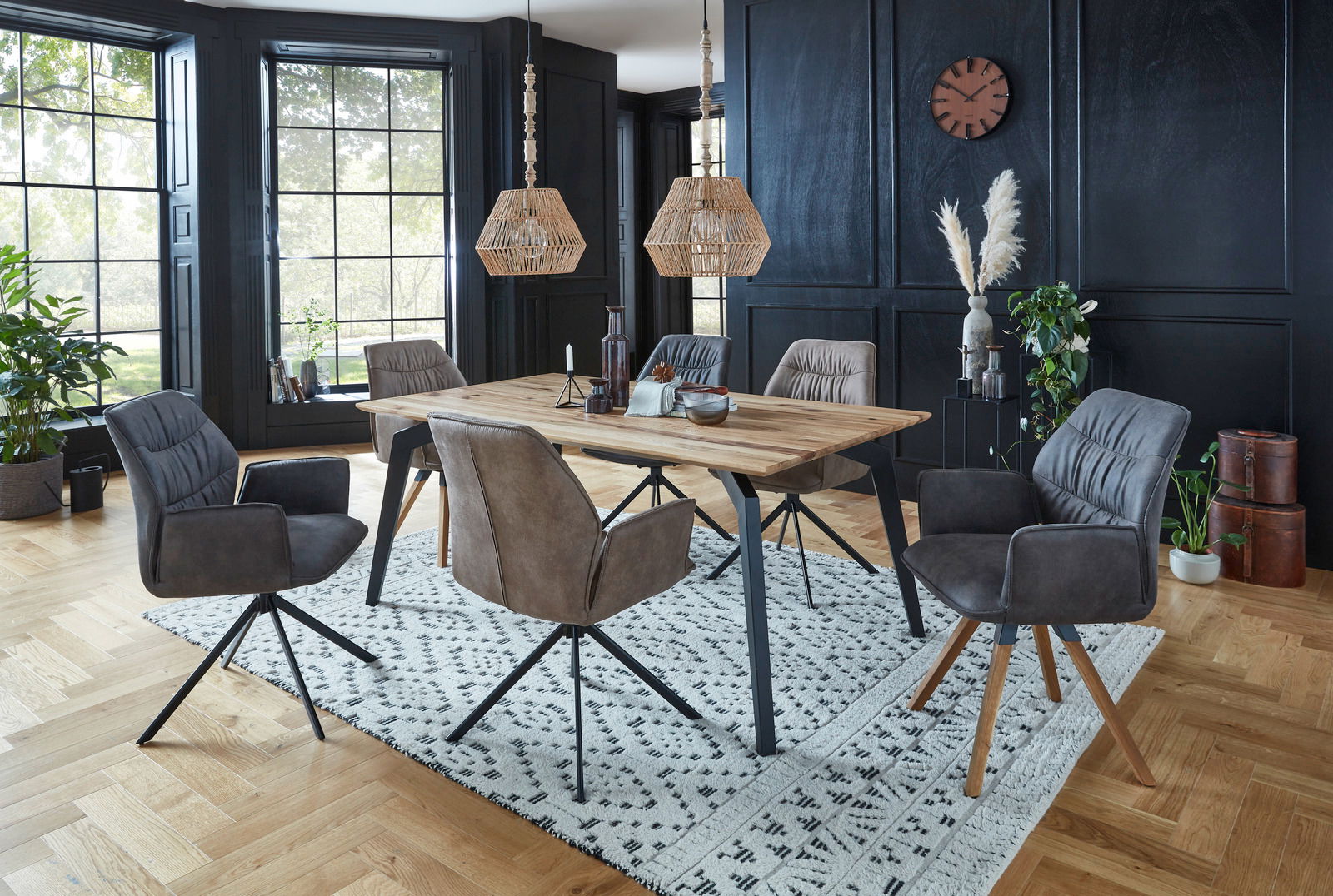 Esszimmer mit modernem Esstisch aus Holz und sechs gepolsterten Sesseln der Serie TORTILLA in einem stilvollen Raum mit großen Fenstern und schwarzer Wandverkleidung, seitliche Perspektive.