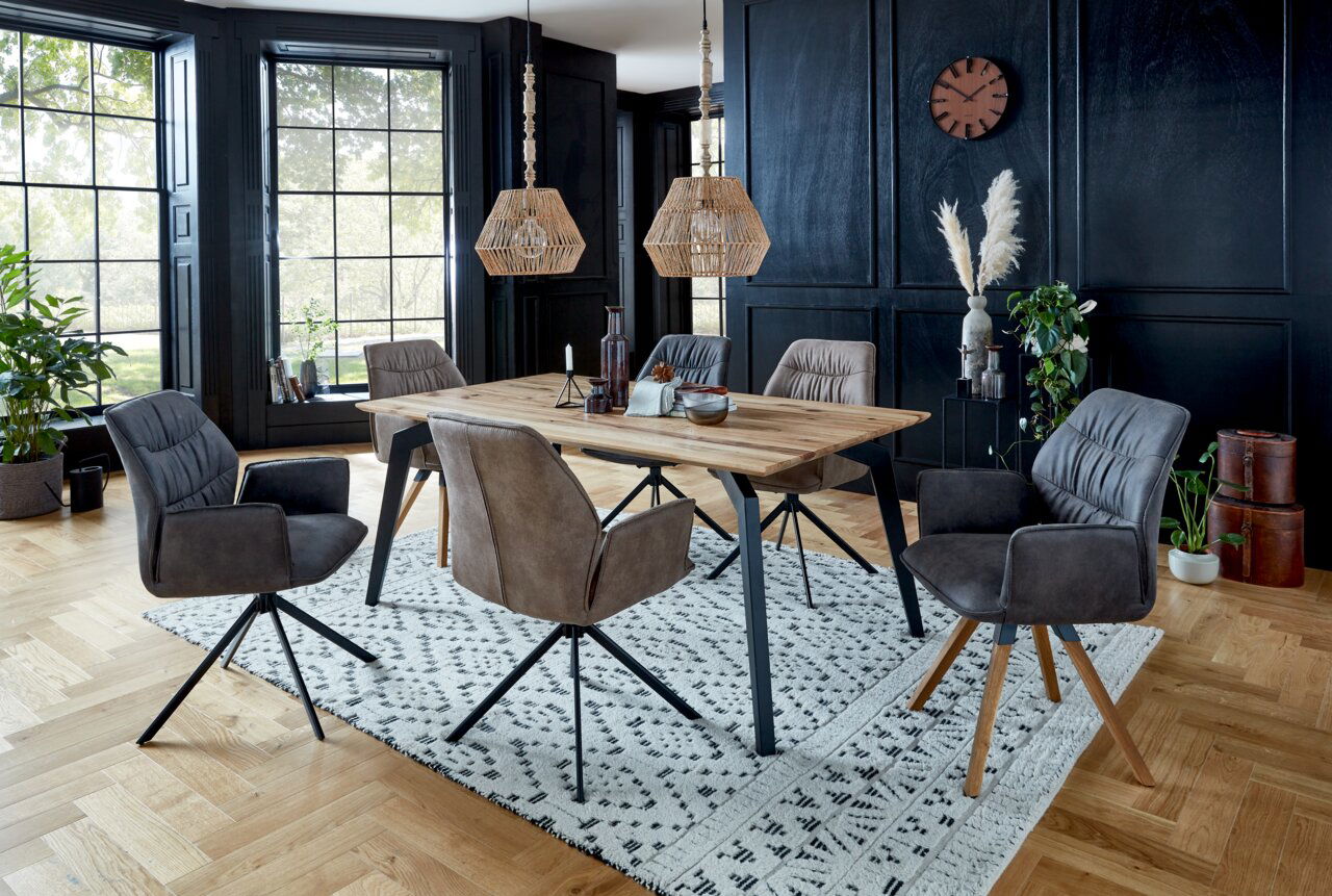 Esszimmer mit modernem Esstisch aus Holz und sechs gepolsterten Sesseln der Serie TORTILLA in einem stilvollen Raum mit großen Fenstern und schwarzer Wandverkleidung, seitliche Perspektive.