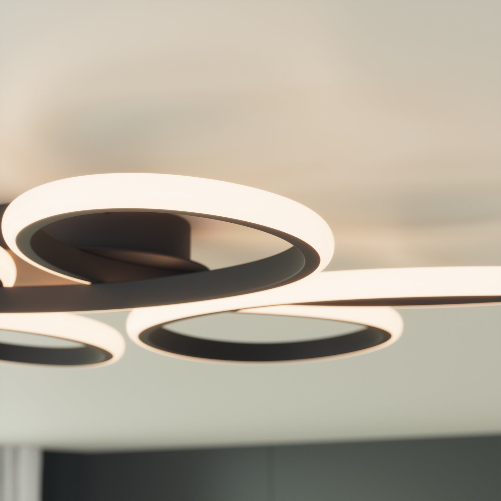 Moderne LED-Deckenleuchte mit drei leuchtenden Ring-Elementen in Schwarz und warmweißem Licht, fotografiert aus leichter Untersicht in Innenraum-Umgebung