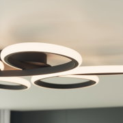 Moderne LED-Deckenleuchte mit drei leuchtenden Ring-Elementen in Schwarz und warmweißem Licht, fotografiert aus leichter Untersicht in Innenraum-Umgebung