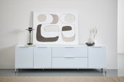 Frontale Ansicht eines modernen, weißen Sideboards mit Metalluntergestell, dekoriert mit einer abstrakten Kunstleinwand, einer schwarzen Lampe, einem Buch, einer Vase und einer Schale.