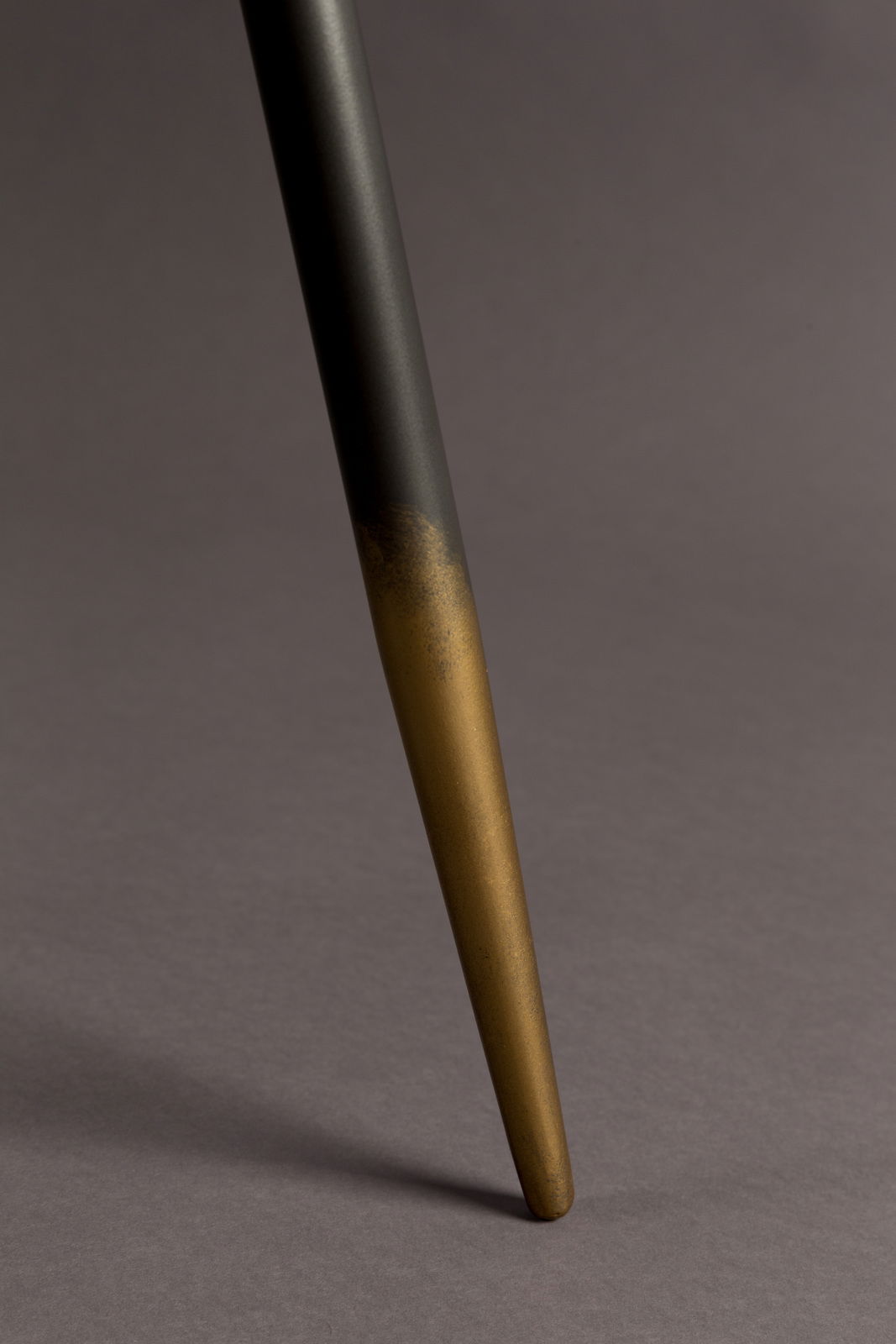 Nahaufnahme eines Tischbeins mit schwarzer und goldener Farbgebung, schräg von der Seite fotografiert.