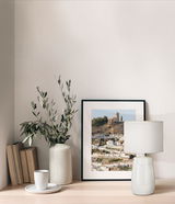 Tischleuchte Face in einem modernen Interieur, seitliche Perspektive, neben einem gerahmten Bild und einer Vase mit Zweigen auf einem Holztisch.