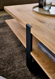 Detailaufnahme aus schräger Seitenperspektive: moderner Couchtisch mit massiver Holzplatte und Ablage, schwarzem Metallgestell und Tablett mit Glas auf der Oberfläche