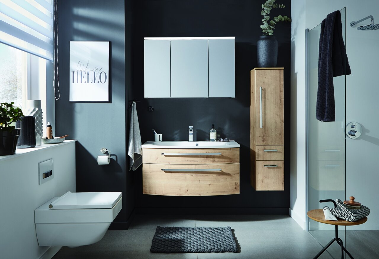 Moderne Badezimmeransicht mit einem hängenden Waschtisch in Holzoptik, einem großen Spiegel und einem hohen Schrank, aufgenommen aus einer frontalen Perspektive.