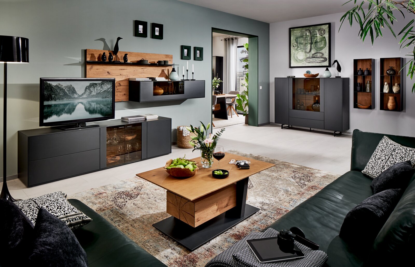 Moderne woonkamerwandcombinatie in donkere tinten met houten accenten, bestaande uit een tv-kast, hangkasten en decoraties, gezien vanuit een gezellige woonkamer.