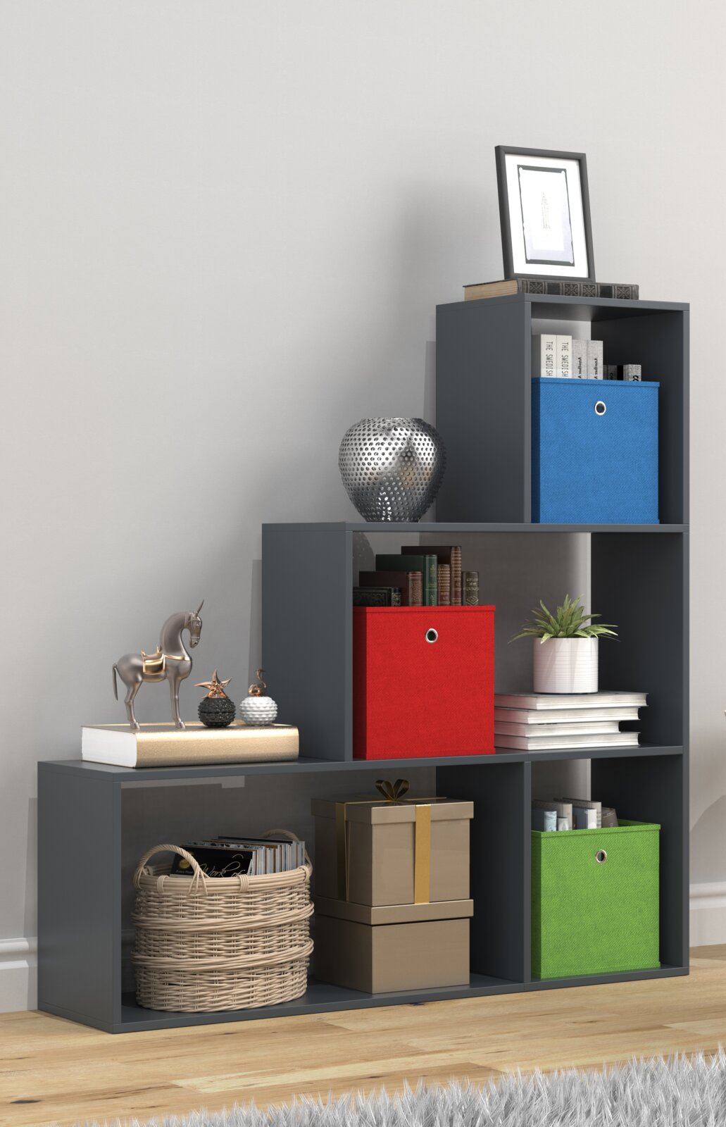 Modernes, dunkelgraues Stufenregal mit offenen Fächern und farbigen Aufbewahrungsboxen (blau, rot, grün) sowie Deko und Büchern, fotografiert in leichter Seitenansicht von vorne.