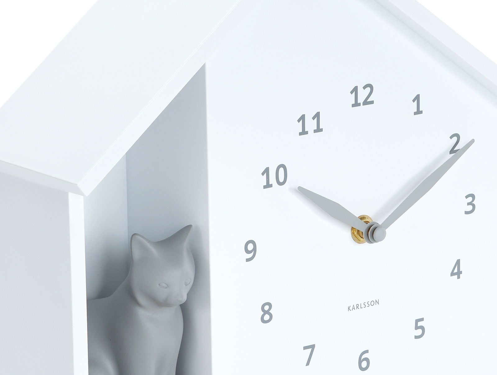 Weiße Wanduhr mit einem minimalistischen Design, das eine graue Katzenfigur in einem seitlichen Fach zeigt. Die Uhr hat schwarze Ziffern und Zeiger. Perspektive: seitliche Ansicht.