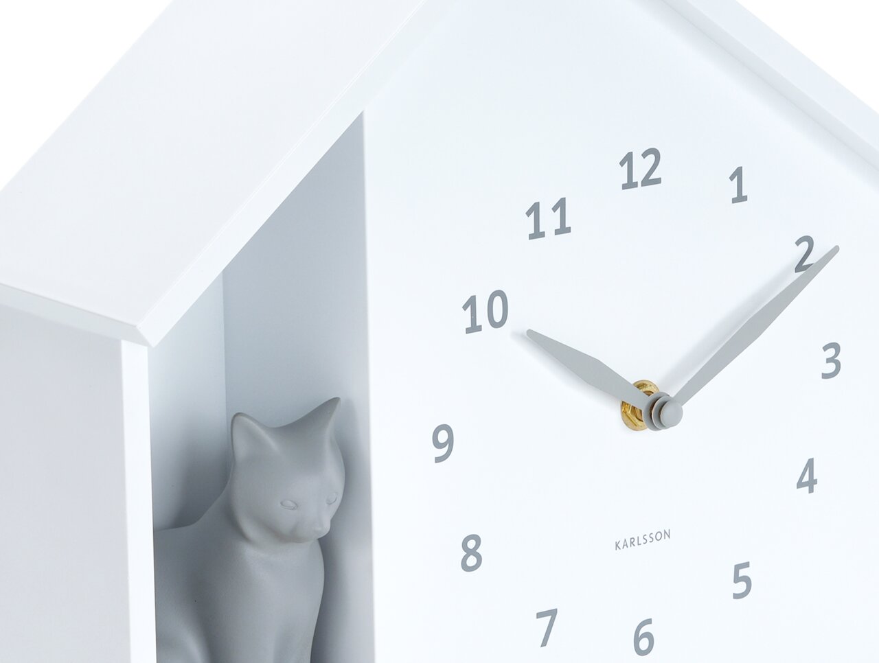 Witte wandklok met een minimalistisch ontwerp, met een grijs kattenfiguurtje in een vakje aan de zijkant. De klok heeft zwarte cijfers en wijzers. Perspectief: zijaanzicht.