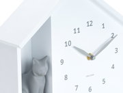 Witte wandklok met een minimalistisch ontwerp, met een grijs kattenfiguurtje in een vakje aan de zijkant. De klok heeft zwarte cijfers en wijzers. Perspectief: zijaanzicht.