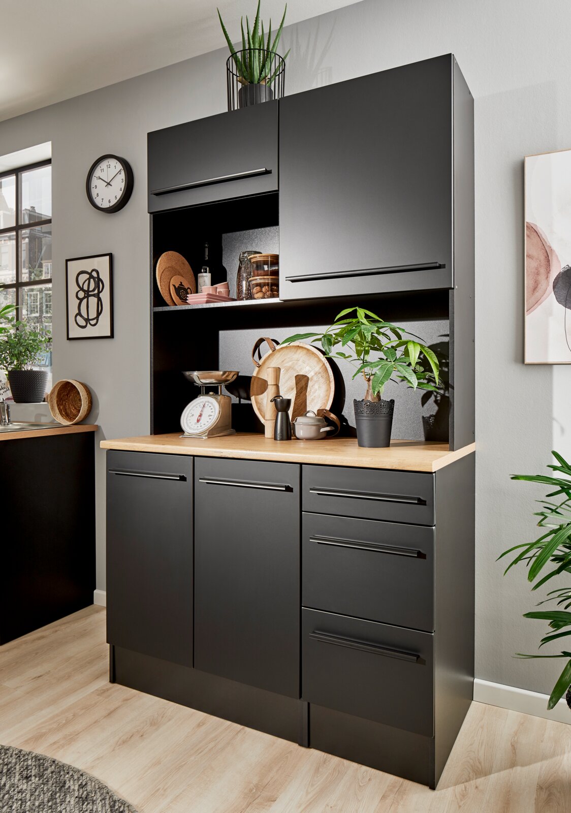 Moderne zwarte buffetkast met houten werkblad, versierd met planten en keukengerei, gezien vanuit het vooraanzicht.