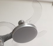 Moderner Deckenventilator mit integrierter runder LED-Leuchte und transparenten Flügeln in Silber/Weiß, von unten aus leichter Untersicht fotografiert.