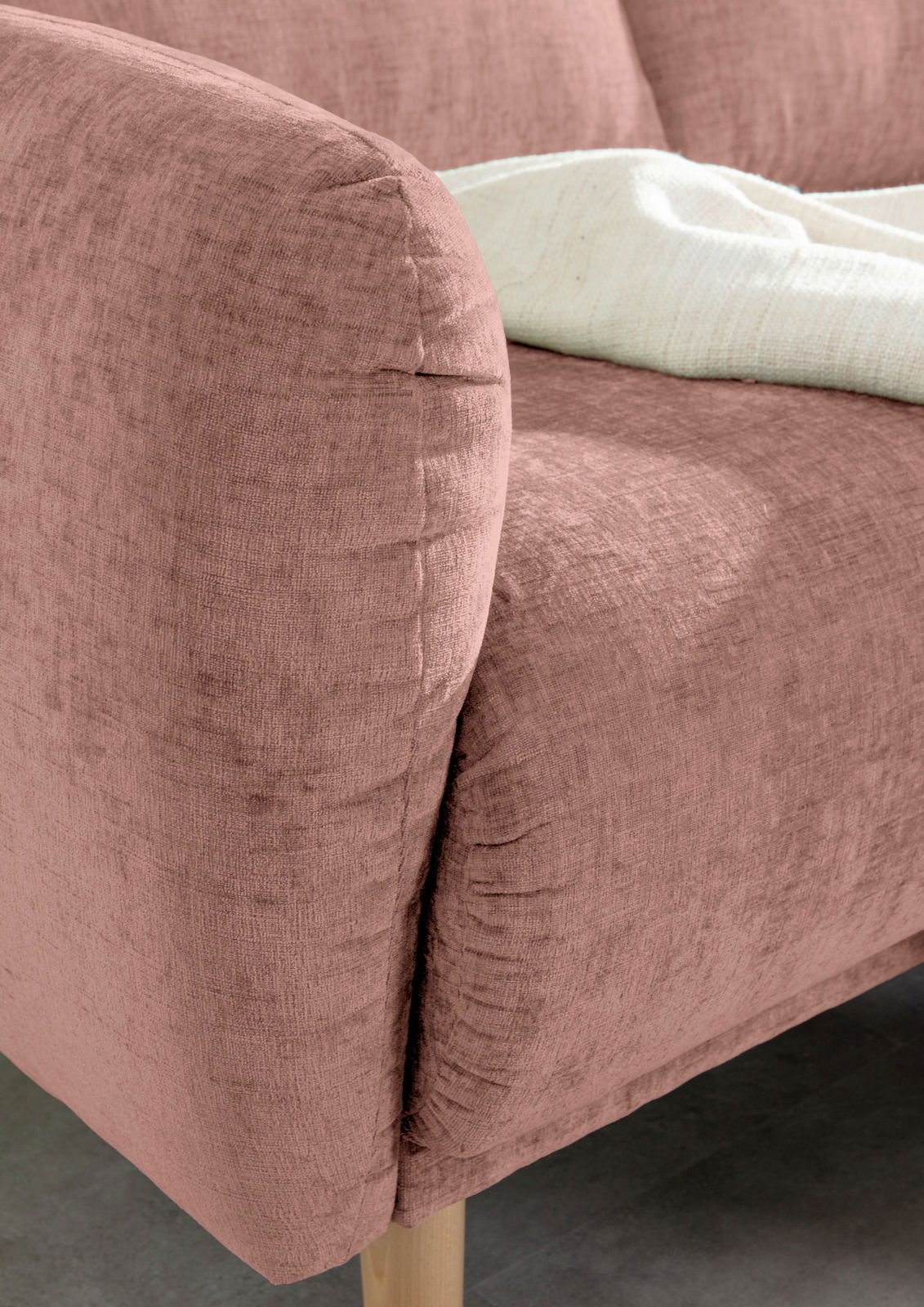 Nahaufnahme einer rosafarbenen Sofaecke mit weicher Textur und Holzfuß, von der Seite betrachtet.